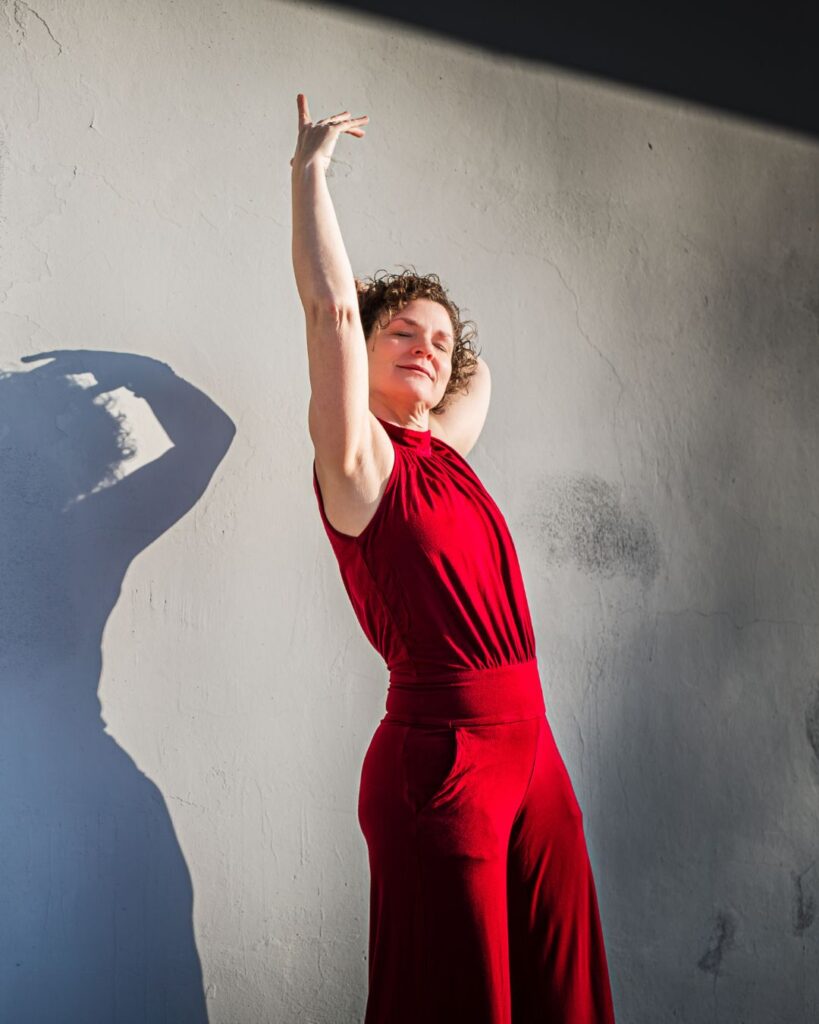 Carolin Limburg steht in rotem Kleid mit erhobenem Arm an einer hellen Wand